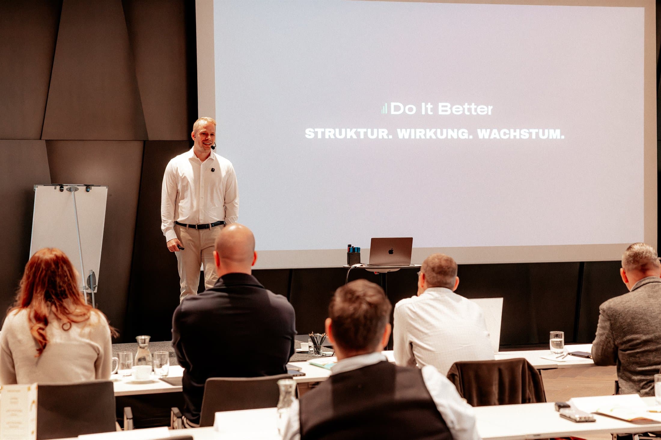 Vortrag vor der Leinwand mit dem Do-It-Better-Leitsatz